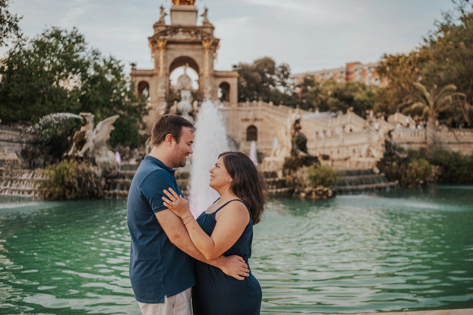 The parents smiling towards one another beside the fountain during their family photoshoot in Barcelona.