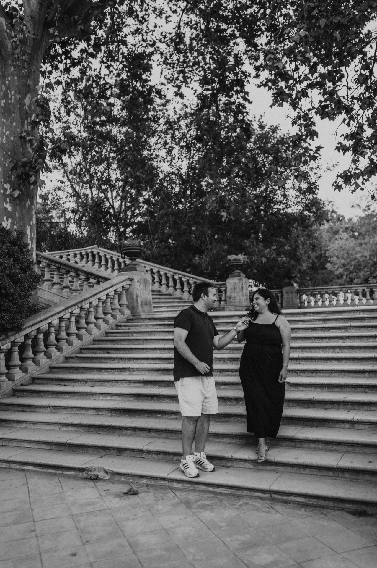 Black-and-white photograph: the parents standing together in front of the broad stone staircase during their family photoshoot in Barcelona.