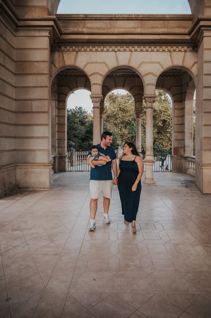 A family walk through the arcade | Barcelona family photoshoot The parents walking together beneath the stone arches while the father carries their child during their family photoshoot in Barcelona.