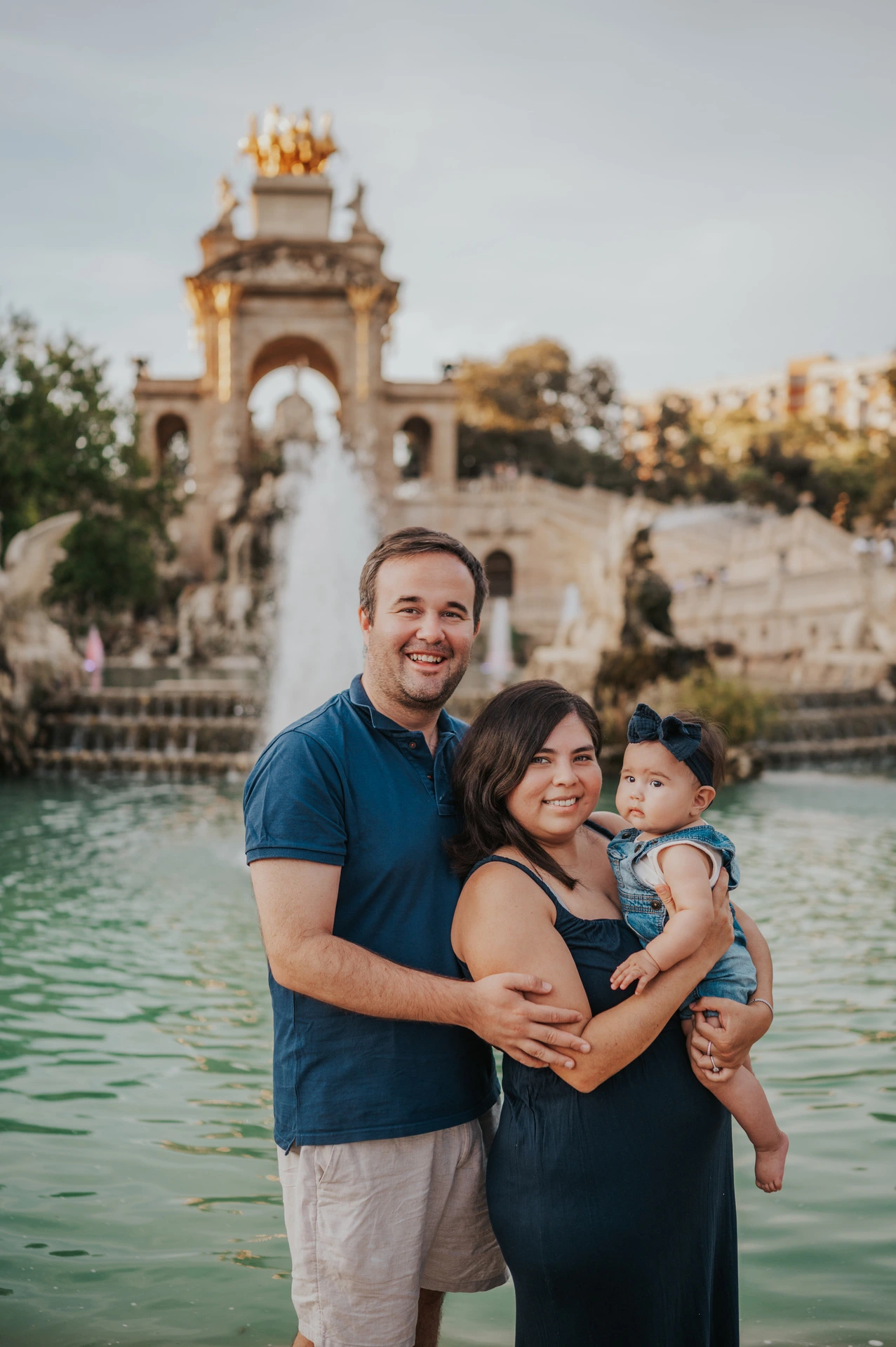 The parents and child smiling together with the fountain behind them during their family photoshoot in Barcelona.
