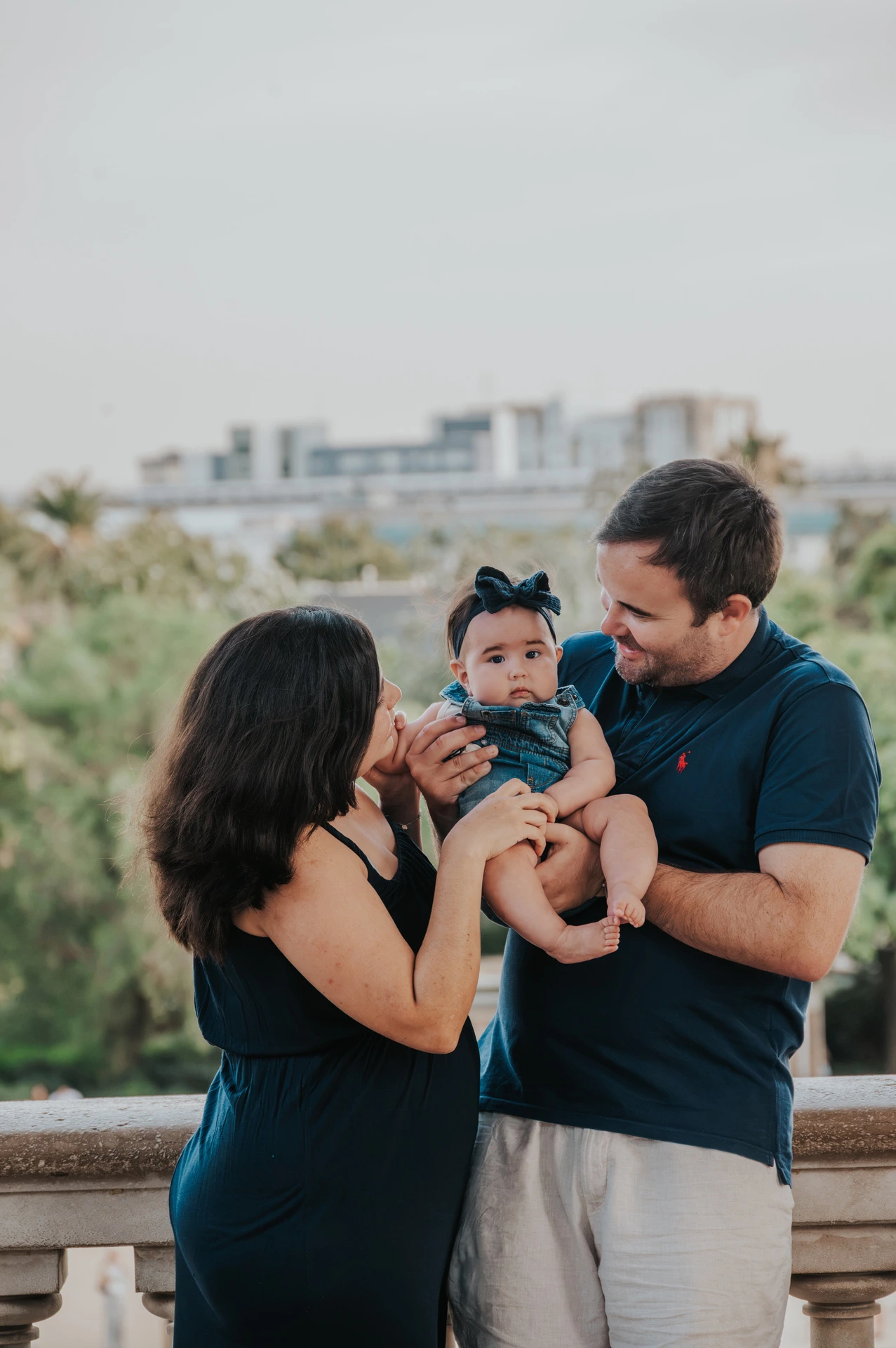 The parents holding their child close beside the water and stone balustrade during their family photoshoot in Barcelona.