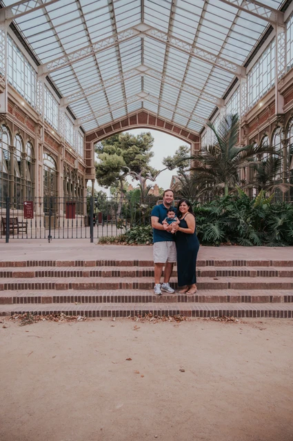 Together beneath the glass roof | Barcelona family photoshoot The family standing together beneath the glass and iron roof among green plants during their family photoshoot in Barcelona.