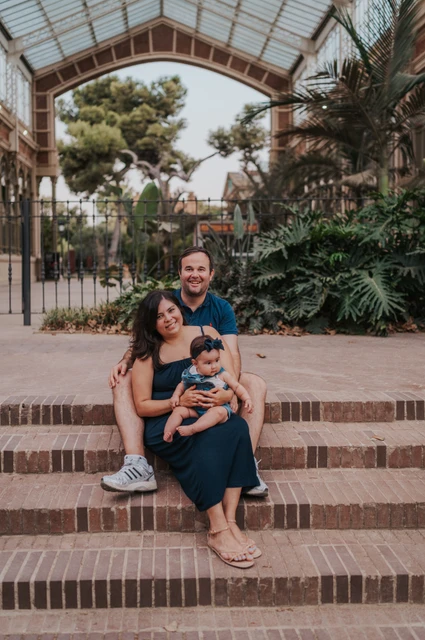 A family portrait on the glasshouse steps | Barcelona family photoshoot The family sitting together on the steps beneath a glass and iron roof during their family photoshoot in Barcelona.