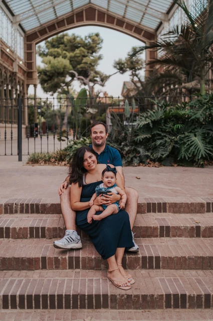 The family sitting together on the steps beneath a glass and iron roof during their family photoshoot in Barcelona.