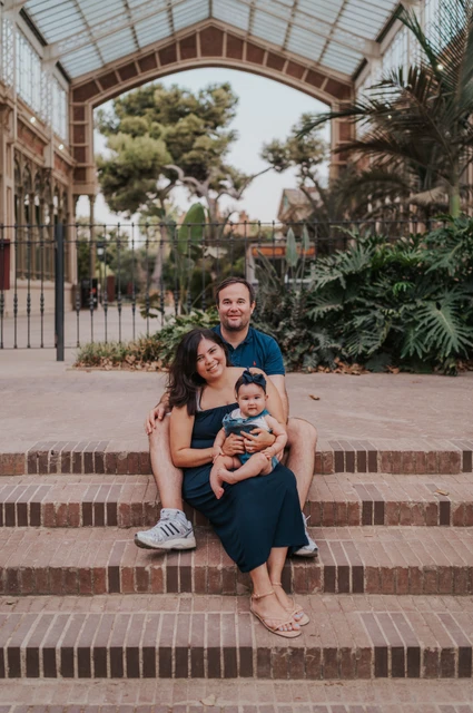 A family portrait on the glasshouse steps | Barcelona family photoshoot The family sitting together on the steps beneath a glass and iron roof during their family photoshoot in Barcelona.
