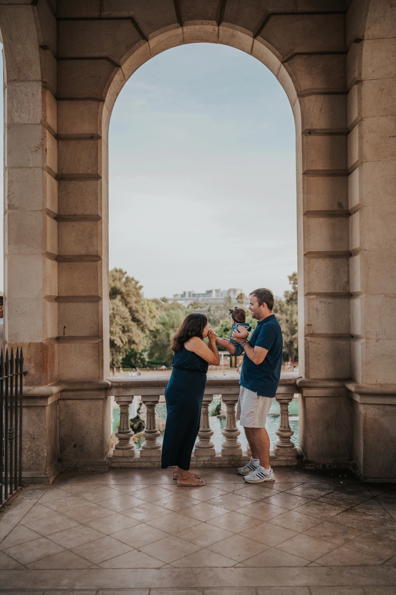 The parents raising their child between them beneath a stone arch during their family photoshoot in Barcelona.