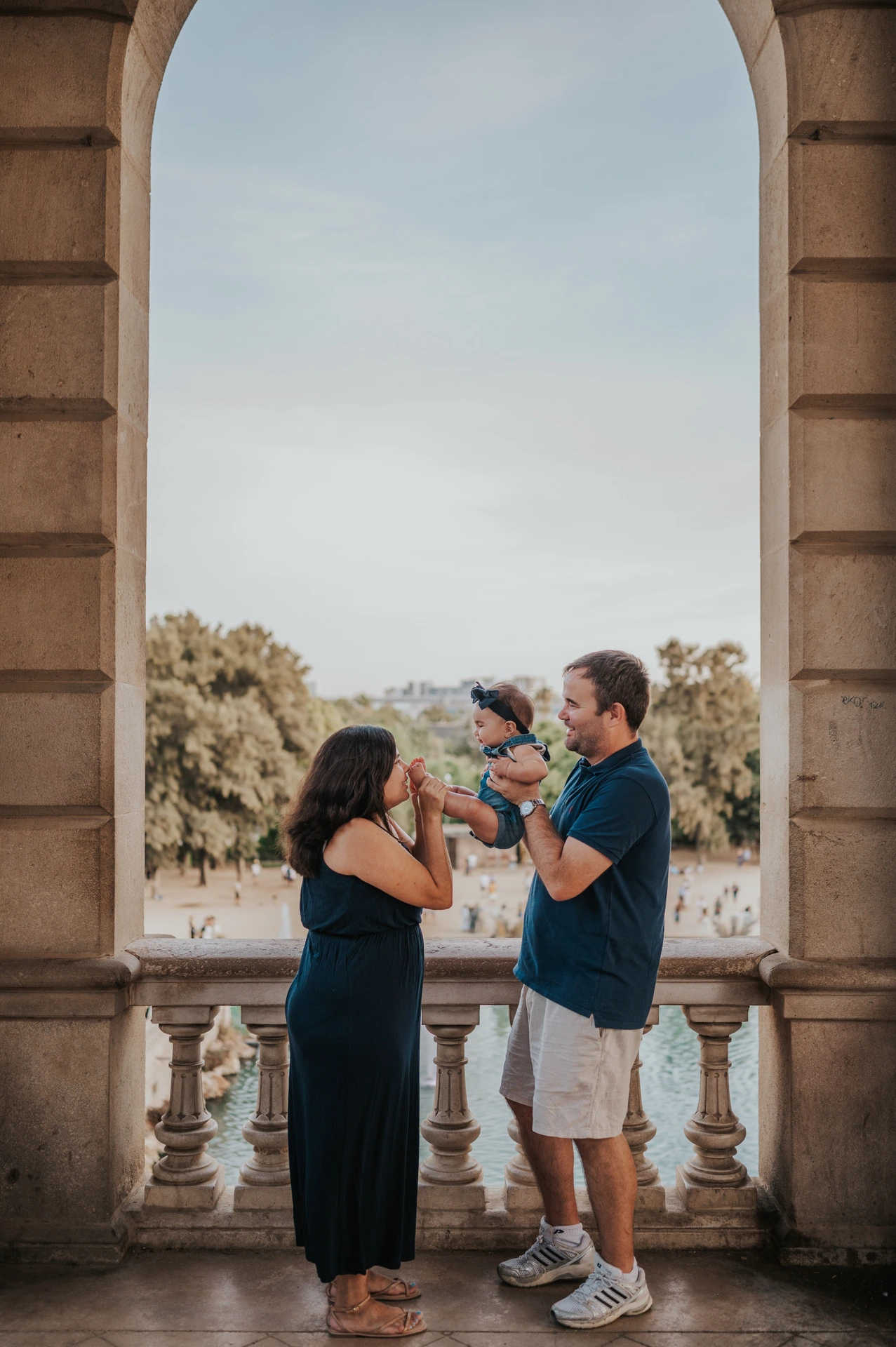 The parents raising their child between them beneath a stone arch during their family photoshoot in Barcelona.