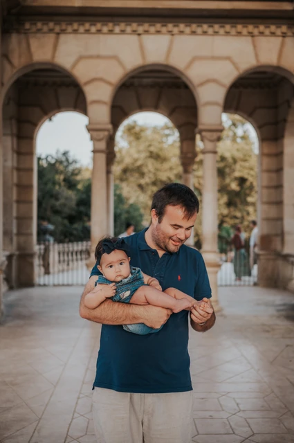 A smile for their child in the arcade | Barcelona family photoshoot The father looking down at the child in his arms beneath the stone arches during their family photoshoot in Barcelona.
