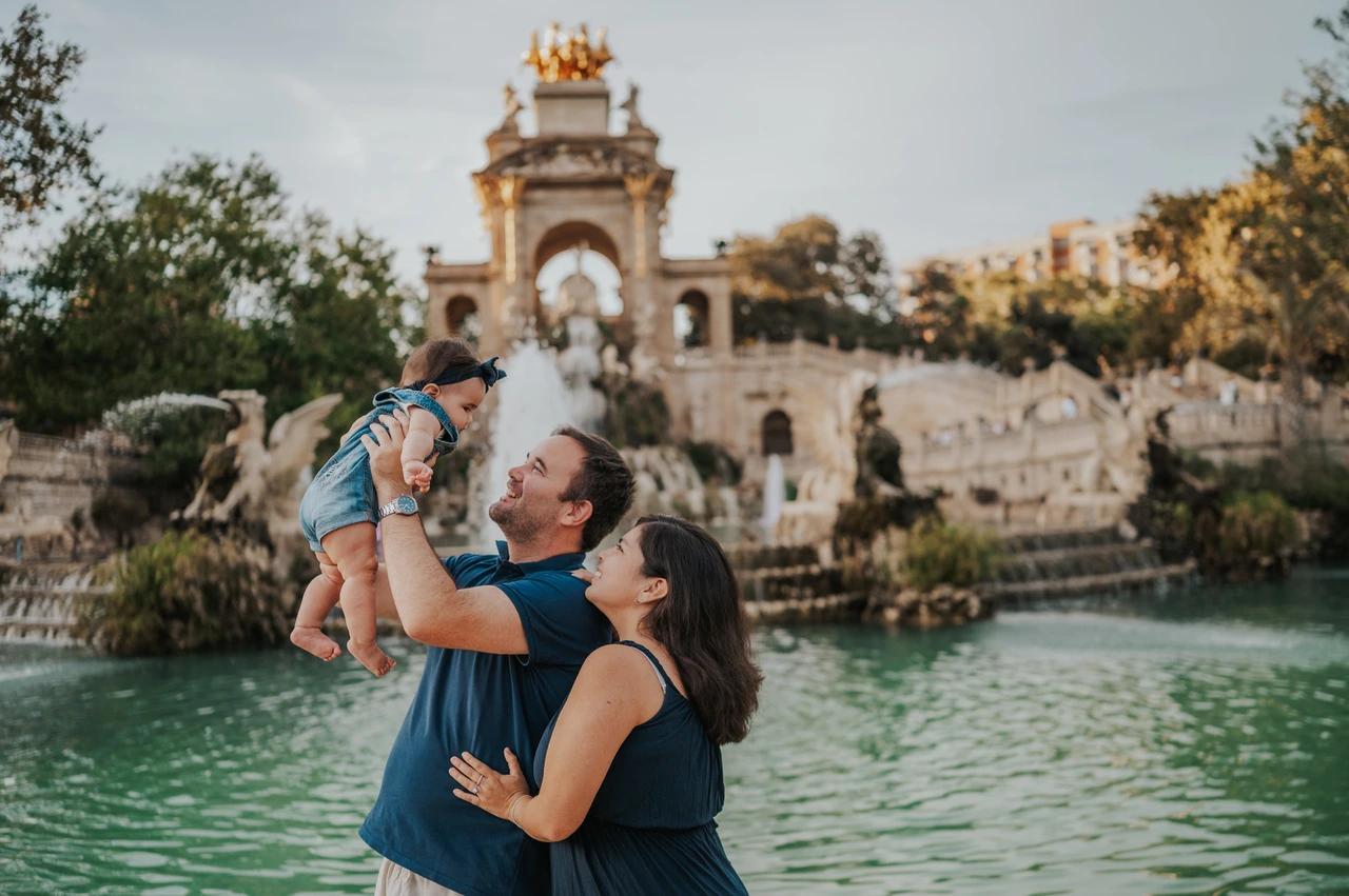 A playful lift by the fountain | Barcelona family photoshoot The father lifting his child while the mother looks up at them beside the fountain during their family photoshoot in Barcelona.