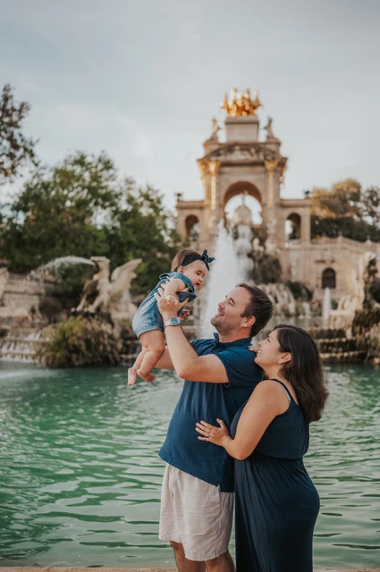A playful lift by the fountain | Barcelona family photoshoot The father lifting his child while the mother looks up at them beside the fountain during their family photoshoot in Barcelona.