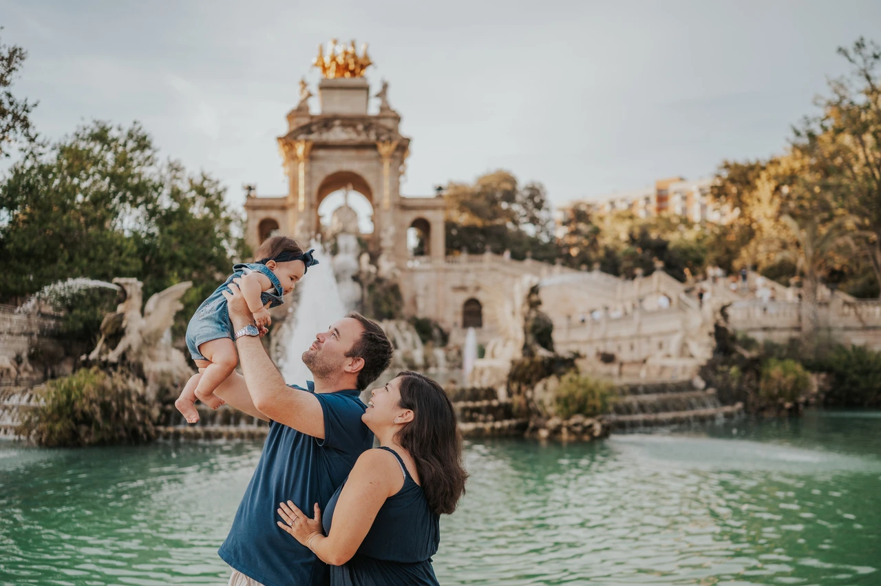 A playful lift by the fountain | Barcelona family photoshoot The father lifting his child while the mother looks up at them beside the fountain during their family photoshoot in Barcelona.