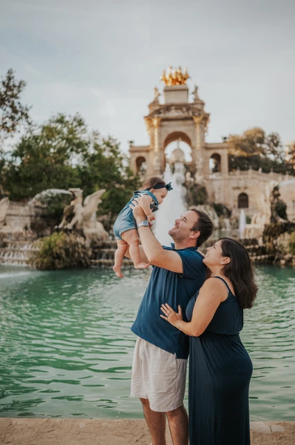 A playful lift by the fountain | Barcelona family photoshoot The father lifting his child while the mother looks up at them beside the fountain during their family photoshoot in Barcelona.