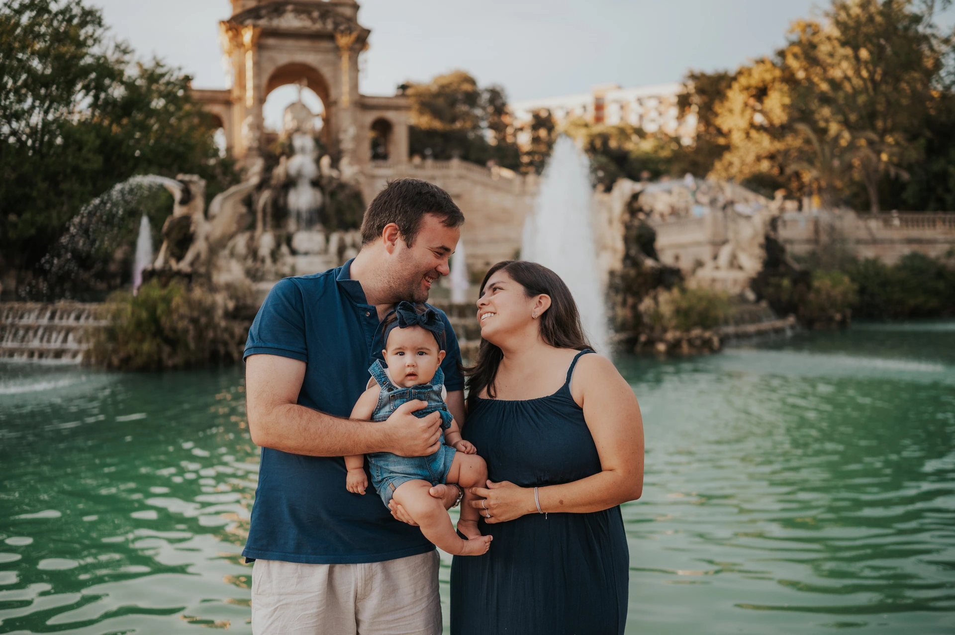 The parents turning towards each other and their child beside the fountain during their family photoshoot in Barcelona.