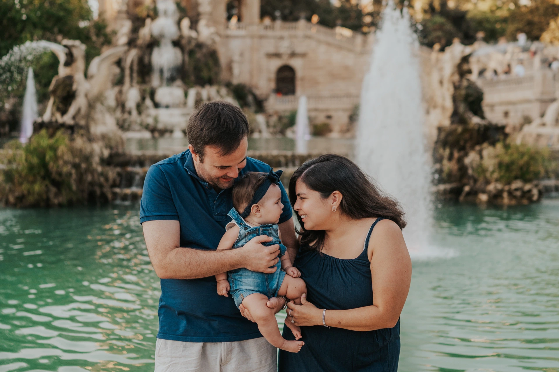 The parents turning towards each other and their child beside the fountain during their family photoshoot in Barcelona.