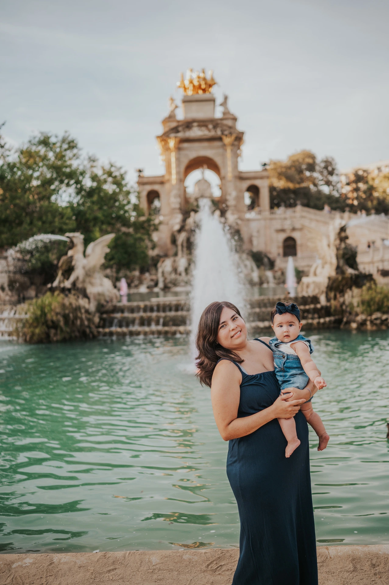 The mother holding her child in front of the green fountain pool during their family photoshoot in Barcelona.