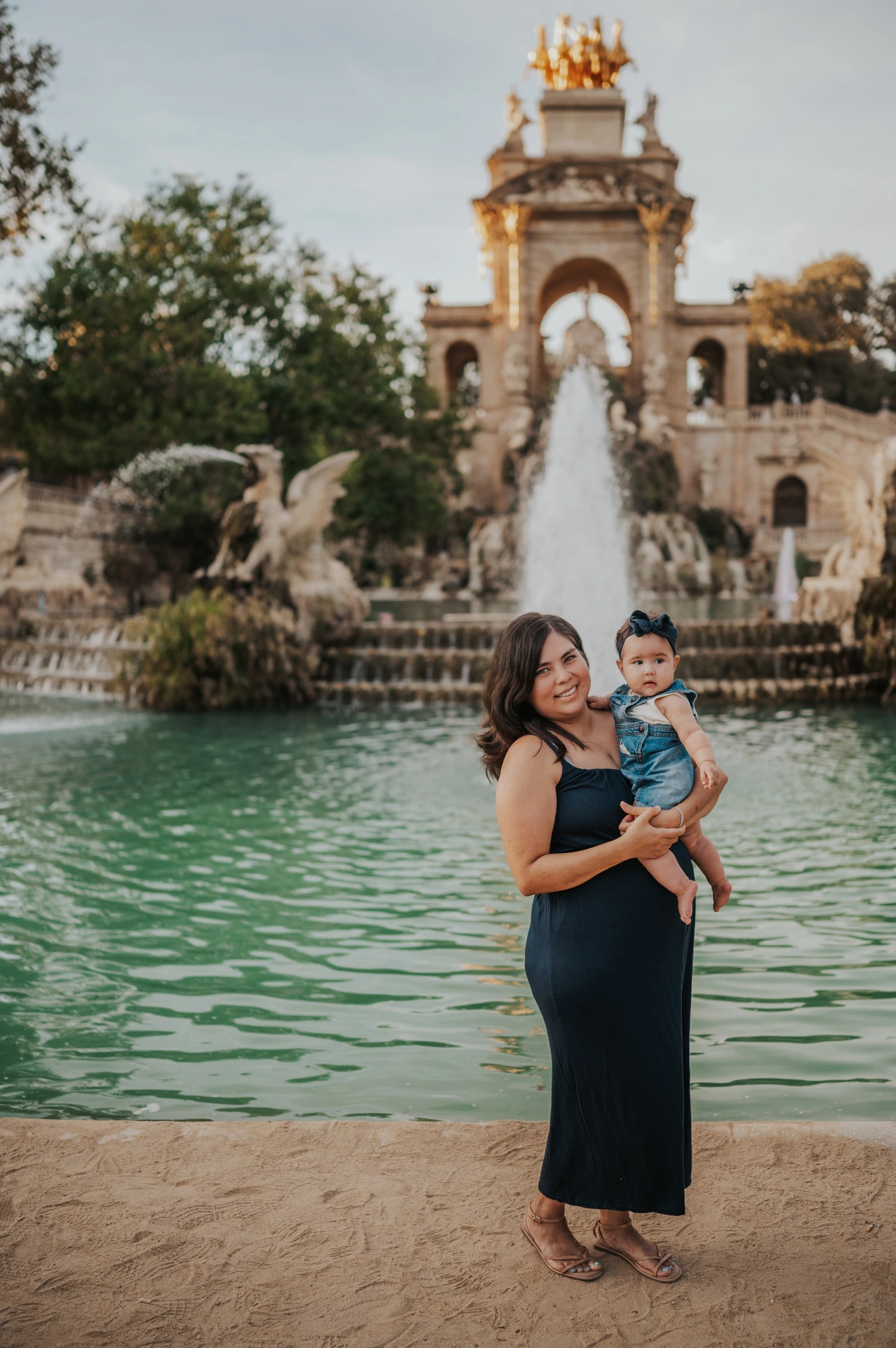 The mother holding her child in front of the green fountain pool during their family photoshoot in Barcelona.