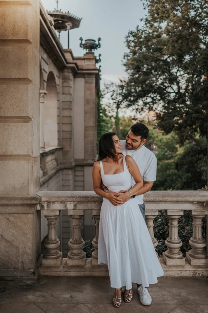 A quiet embrace under the arch | Barcelona engagement photoshoot The couple leaning close together under a stone arch with greenery beyond the railing during their engagement photoshoot in Barcelona.