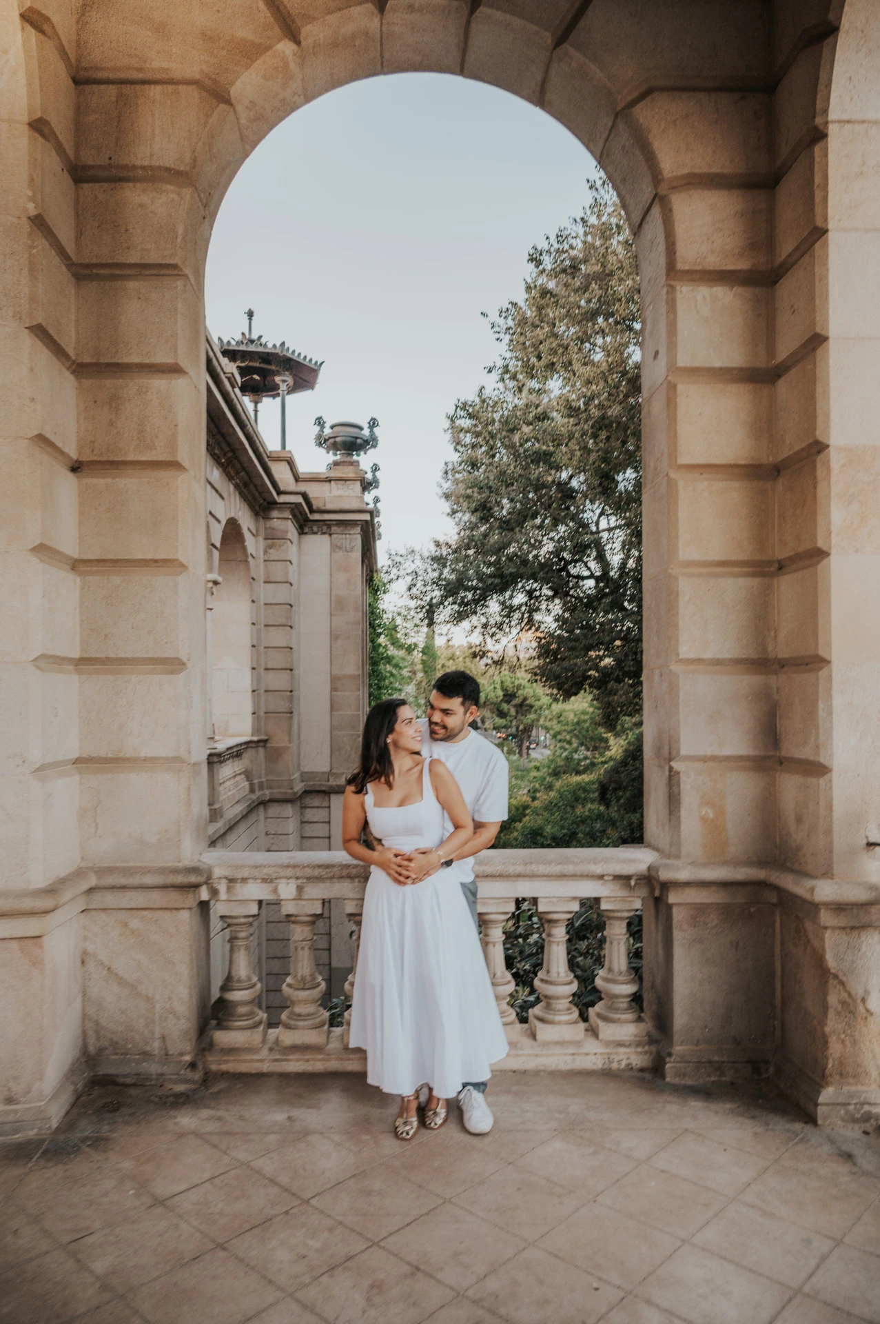 A full-length portrait of the couple holding each other in a tall stone archway during their engagement photoshoot in Barcelona.