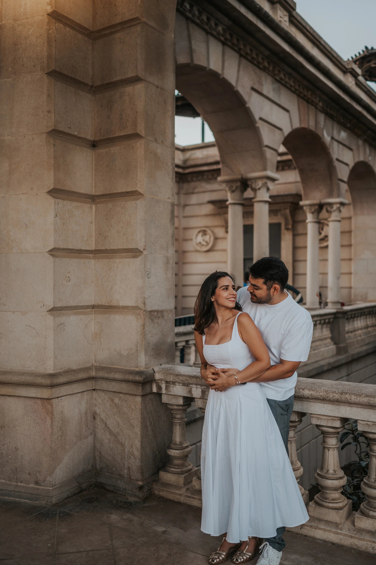 The couple standing close together beside the stone arches and balustrade during their engagement photoshoot in Barcelona.