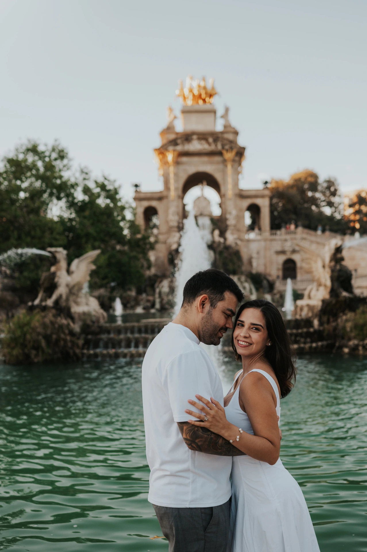 The couple holding each other in front of the fountain, with the woman turning towards the camera during their engagement photoshoot in Barcelona.