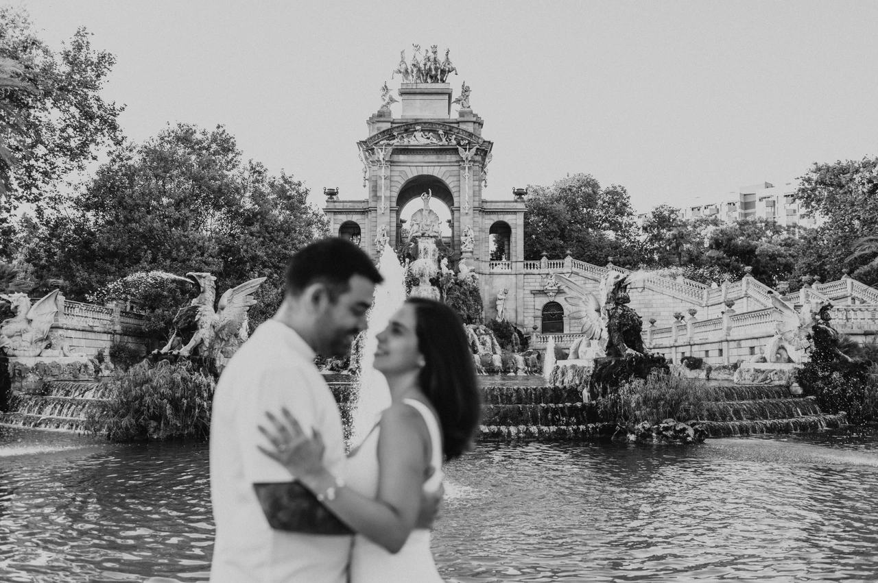 A portrait facing each other by the fountain in black and white | Barcelona engagement photoshoot Black-and-white photograph: the couple facing each other in front of the fountain and its golden-topped arches during their engagement photoshoot in Barcelona.