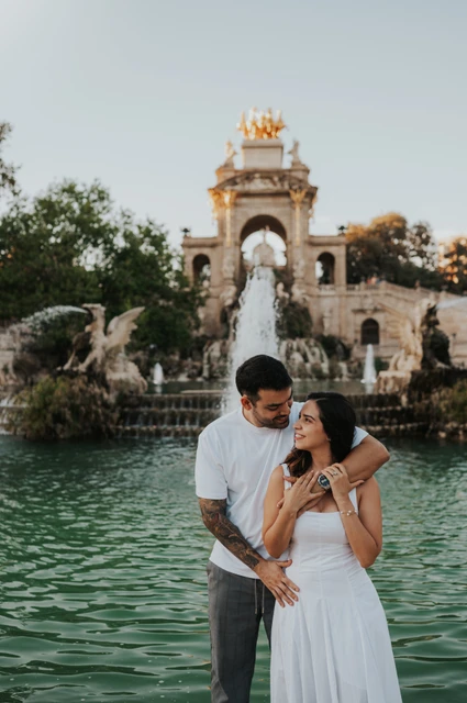 An embrace beside the green pool | Barcelona engagement photoshoot The man with his arm around his partner as they stand together beside the fountain pool during their engagement photoshoot in Barcelona.