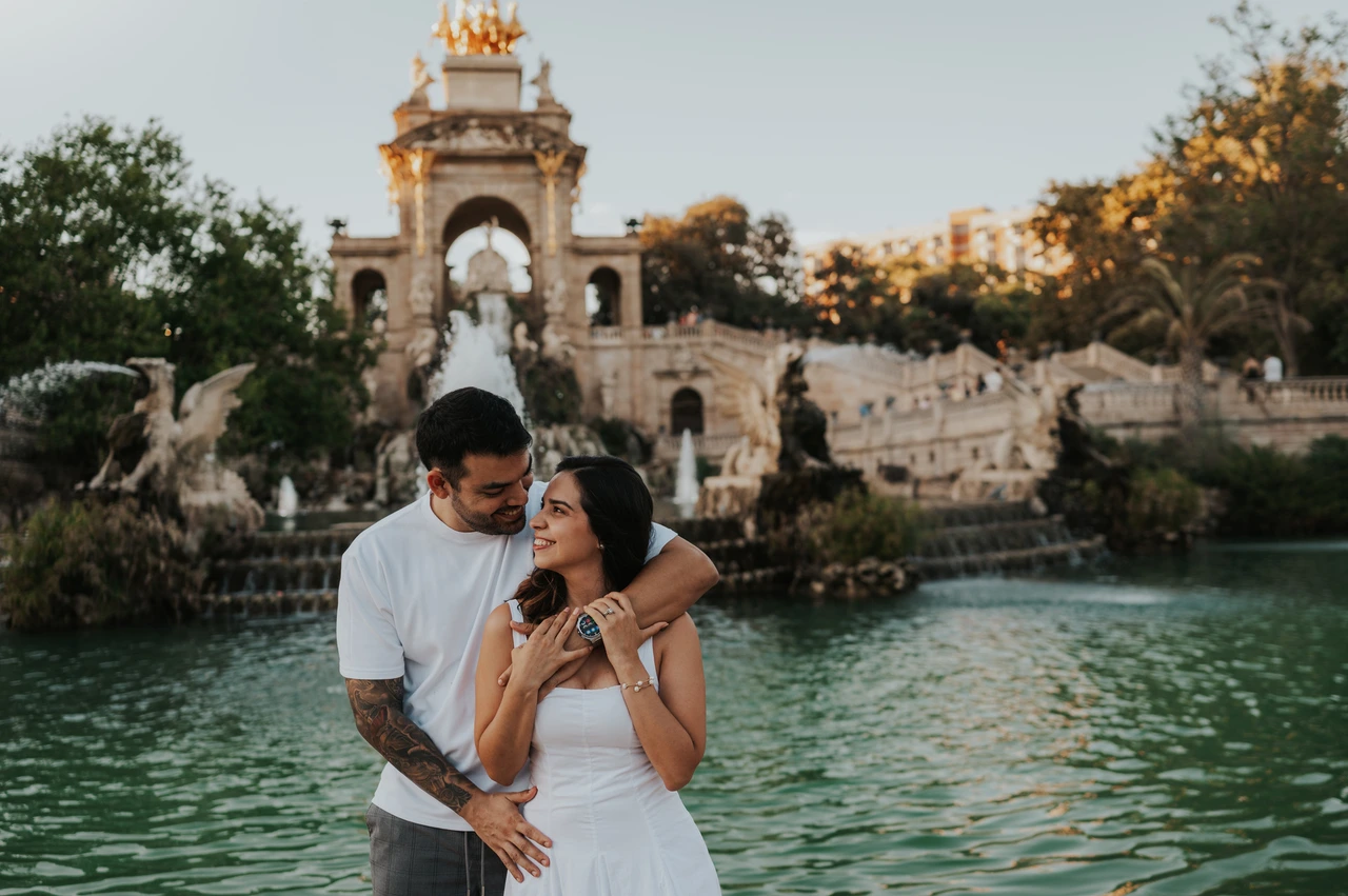An embrace beside the green pool | Barcelona engagement photoshoot The man with his arm around his partner as they stand together beside the fountain pool during their engagement photoshoot in Barcelona.