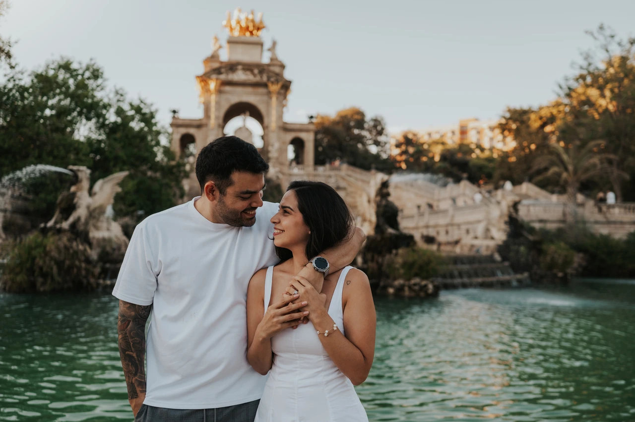 An embrace beside the green pool | Barcelona engagement photoshoot The man with his arm around his partner as they stand together beside the fountain pool during their engagement photoshoot in Barcelona.
