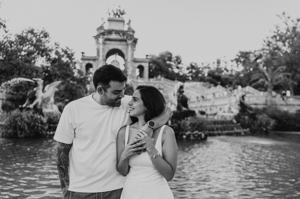 An embrace beside the green pool in black and white | Barcelona engagement photoshoot Black-and-white photograph: the man with his arm around his partner as they stand together beside the fountain pool during their engagement photoshoot in Barcelona.