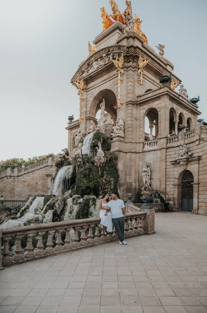 A wide view of the couple beside the fountain’s stone railing and monumental arches during their engagement photoshoot in Barcelona.