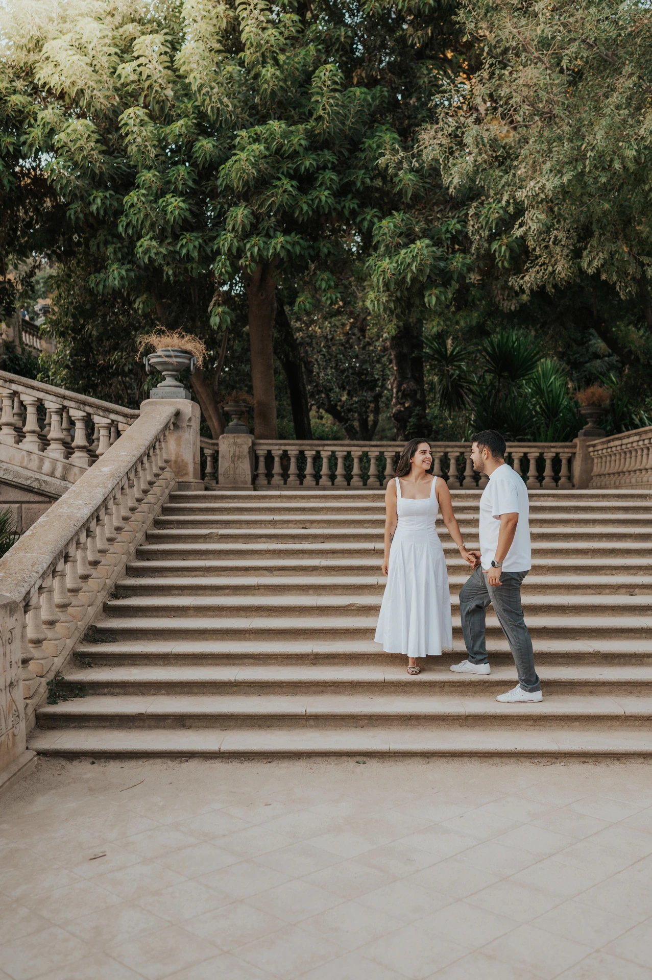 The couple standing together on the broad stone staircase beneath the trees during their engagement photoshoot in Barcelona.