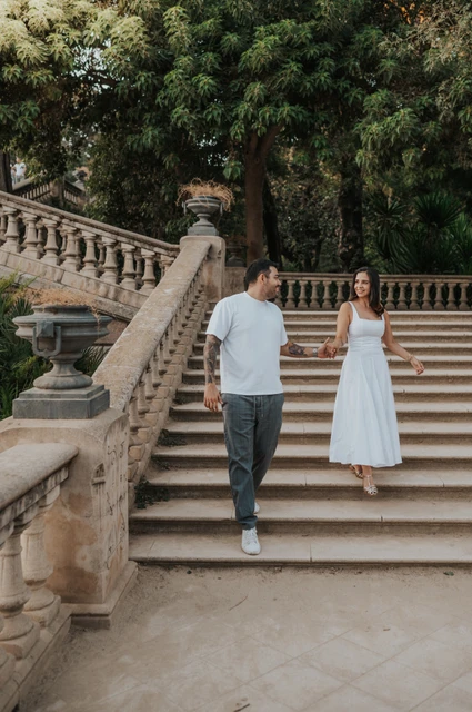 Hand in hand down the park steps | Barcelona engagement photoshoot The couple walking down the broad stone staircase, holding hands beneath leafy trees during their engagement photoshoot in Barcelona.