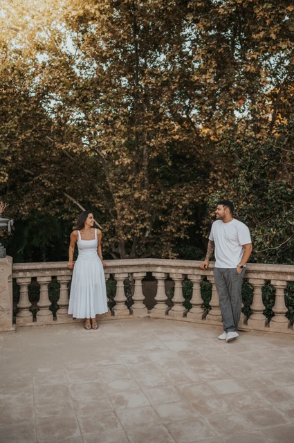 A terrace portrait beneath leafy trees | Barcelona engagement photoshoot The couple standing apart along a stone terrace railing, looking towards each other beneath the trees during their engagement photoshoot in Barcelona.