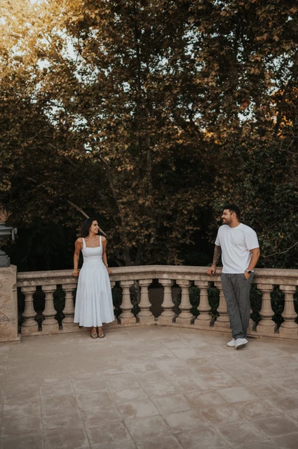 A terrace portrait beneath leafy trees | Barcelona engagement photoshoot The couple standing apart along a stone terrace railing, looking towards each other beneath the trees during their engagement photoshoot in Barcelona.