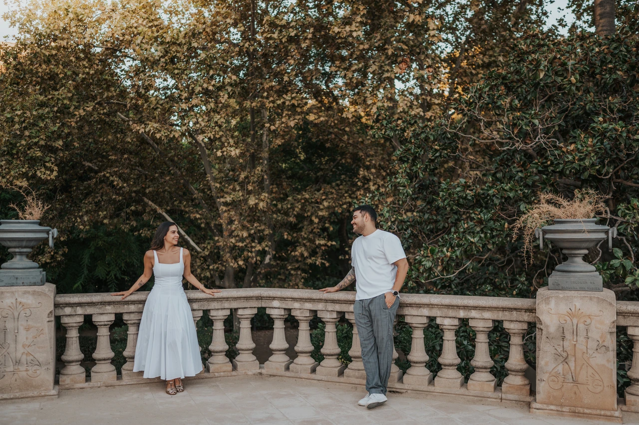 A terrace portrait beneath leafy trees | Barcelona engagement photoshoot The couple standing apart along a stone terrace railing, looking towards each other beneath the trees during their engagement photoshoot in Barcelona.