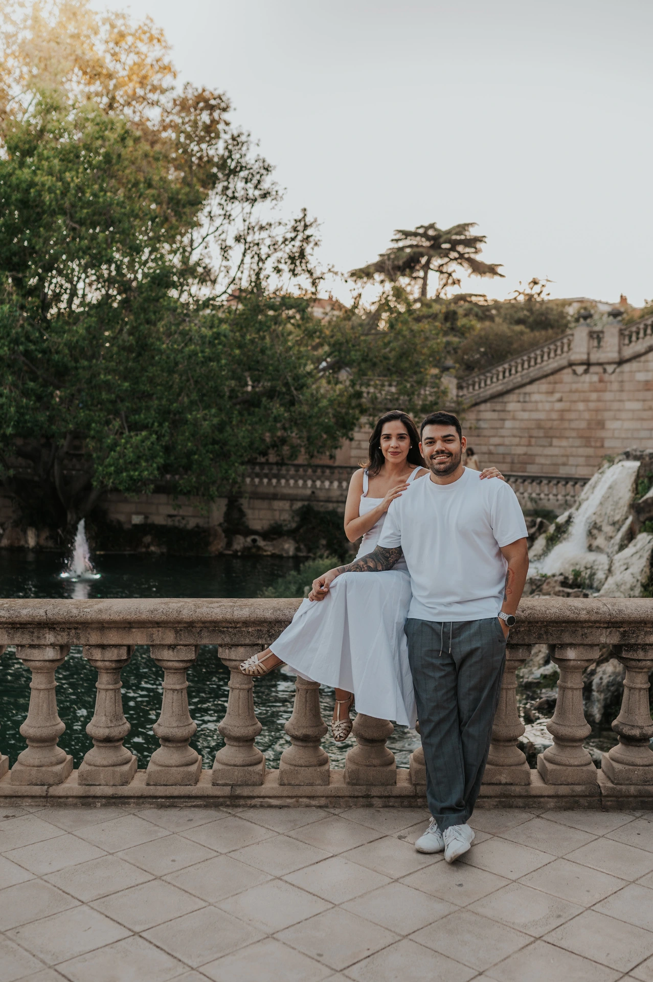 The couple posing by the carved balustrade with the waterfall and fountain architecture behind them during their engagement photoshoot in Barcelona.