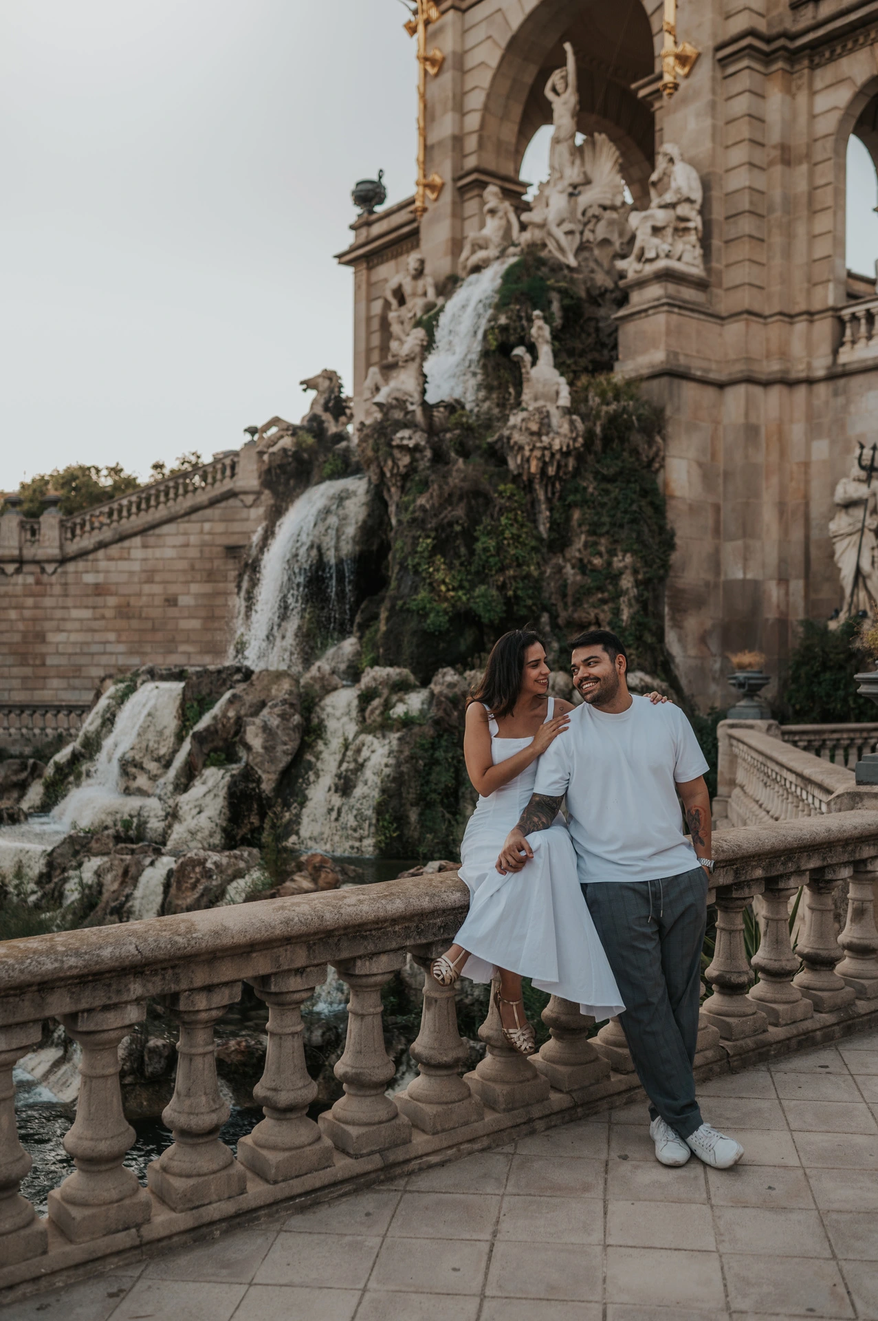 The couple posing by the carved balustrade with the waterfall and fountain architecture behind them during their engagement photoshoot in Barcelona.