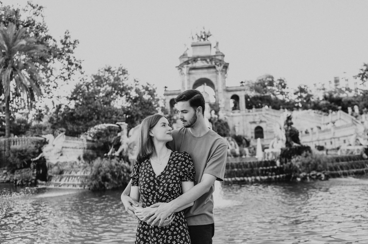 A close embrace beside the green water in black and white | Barcelona couple photoshoot Black-and-white photograph: a closer portrait of the couple embracing beside the green water and ornate park fountain during their couple photoshoot in Barcelona.