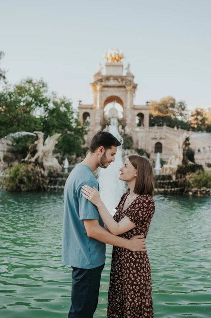 A quiet moment beside the fountain pool | Barcelona couple photoshoot The couple facing each other beside the green fountain pool, with its golden-topped arches behind them during their couple photoshoot in Barcelona.