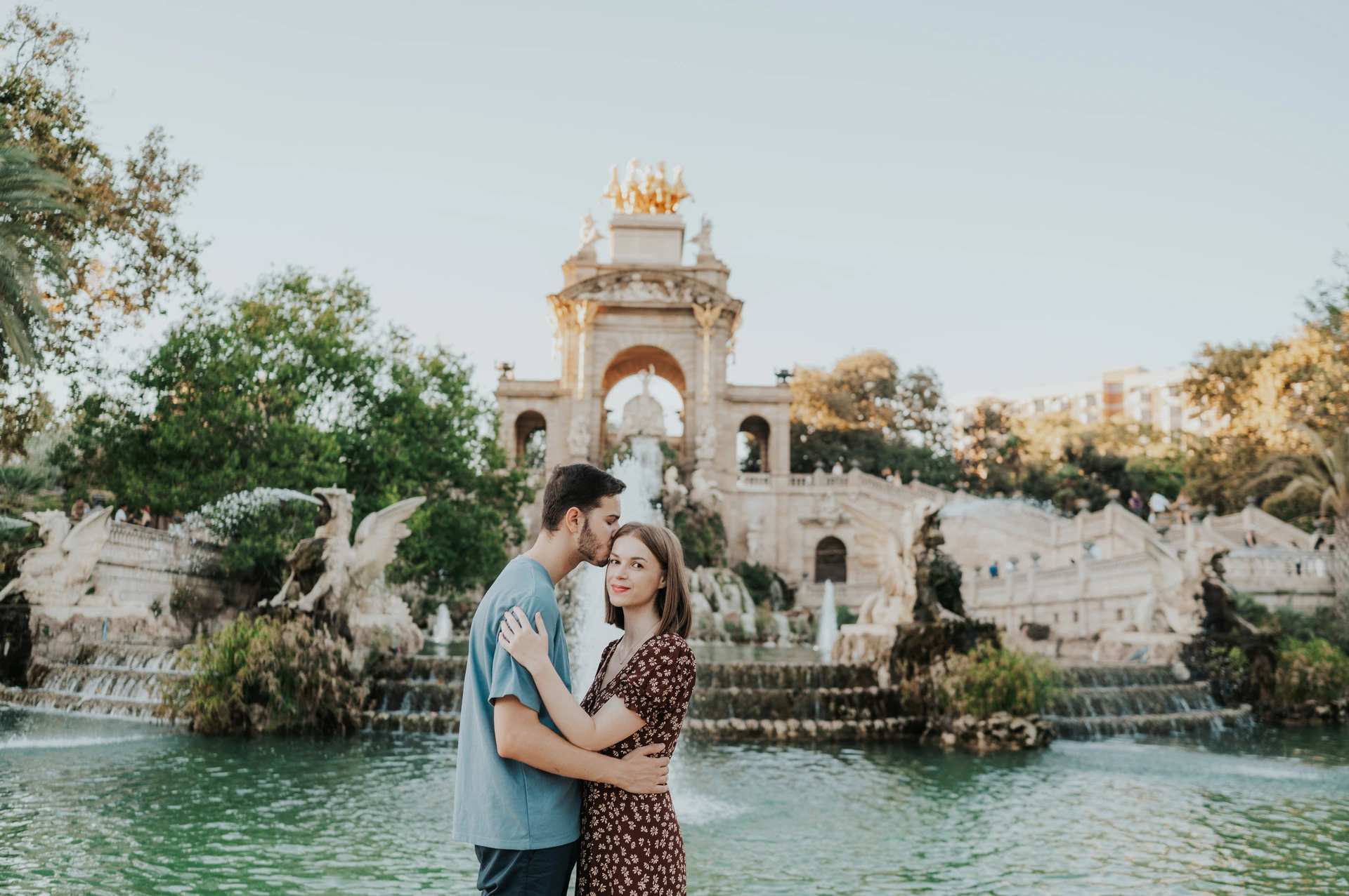The couple holding each other in front of the fountain pool and ornate stone monument during their couple photoshoot in Barcelona.