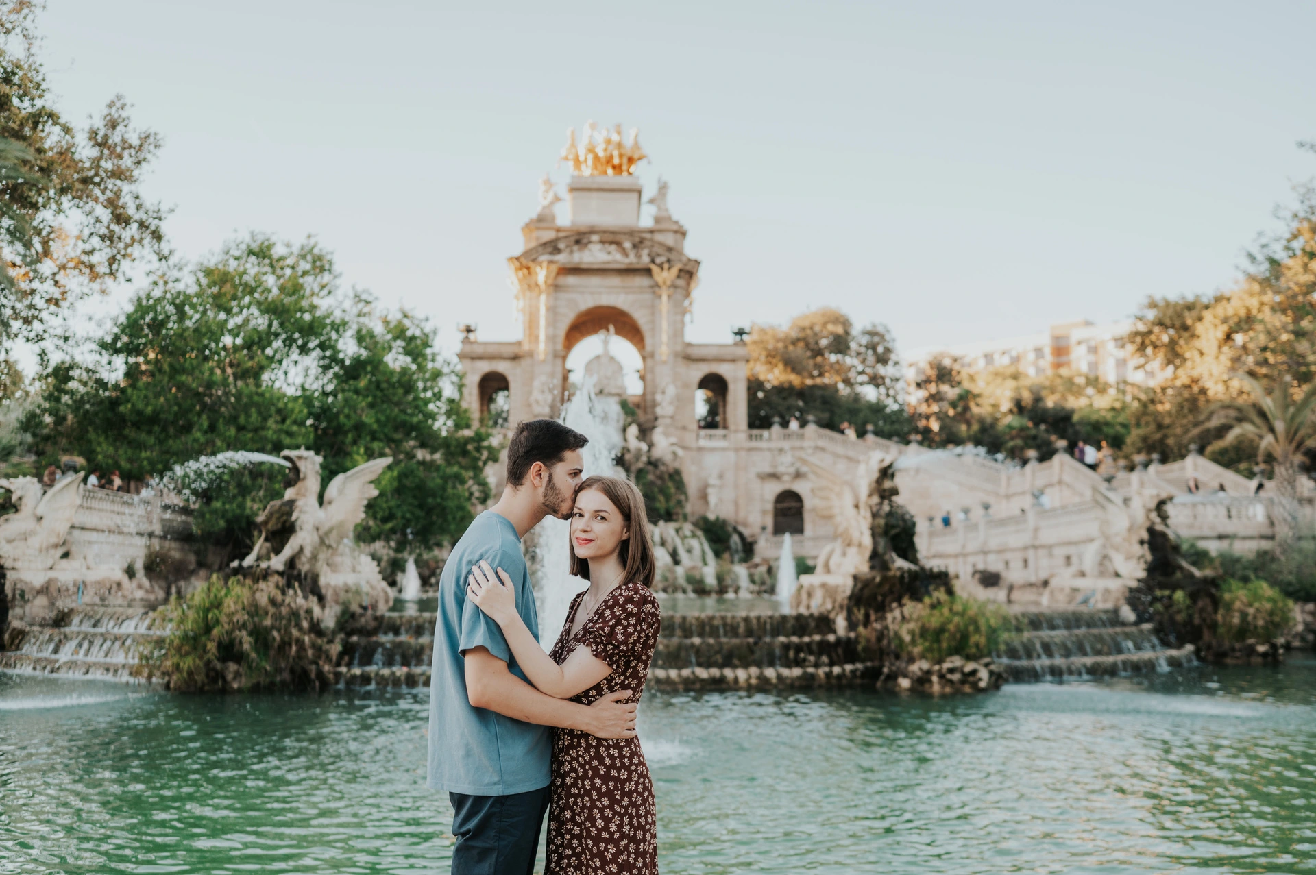The couple holding each other in front of the fountain pool and ornate stone monument during their couple photoshoot in Barcelona.
