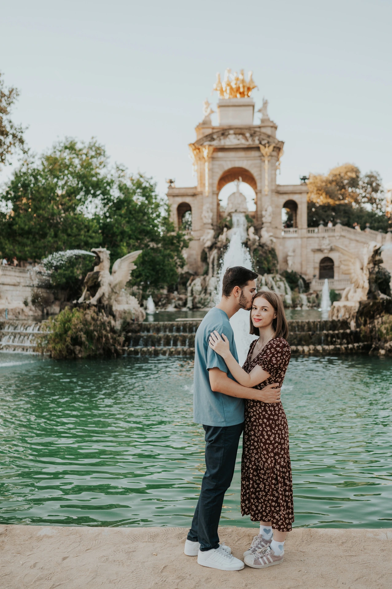 The couple holding each other in front of the fountain pool and ornate stone monument during their couple photoshoot in Barcelona.