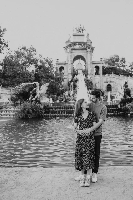 An embrace in front of the fountain in black and white | Barcelona couple photoshoot Black-and-white photograph: the man standing behind his partner and holding her close in front of the park fountain during their couple photoshoot in Barcelona.