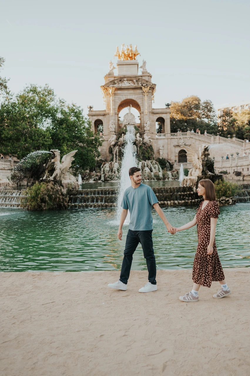 Hand-in-hand portraits by the fountain | Barcelona couple photoshoot The couple holding hands beside the green pool, with the fountain monument in the background during their couple photoshoot in Barcelona.