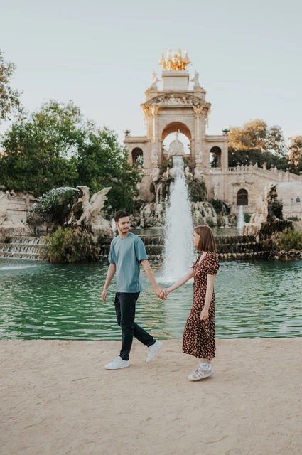 Hand-in-hand portraits by the fountain | Barcelona couple photoshoot The couple holding hands beside the green pool, with the fountain monument in the background during their couple photoshoot in Barcelona.