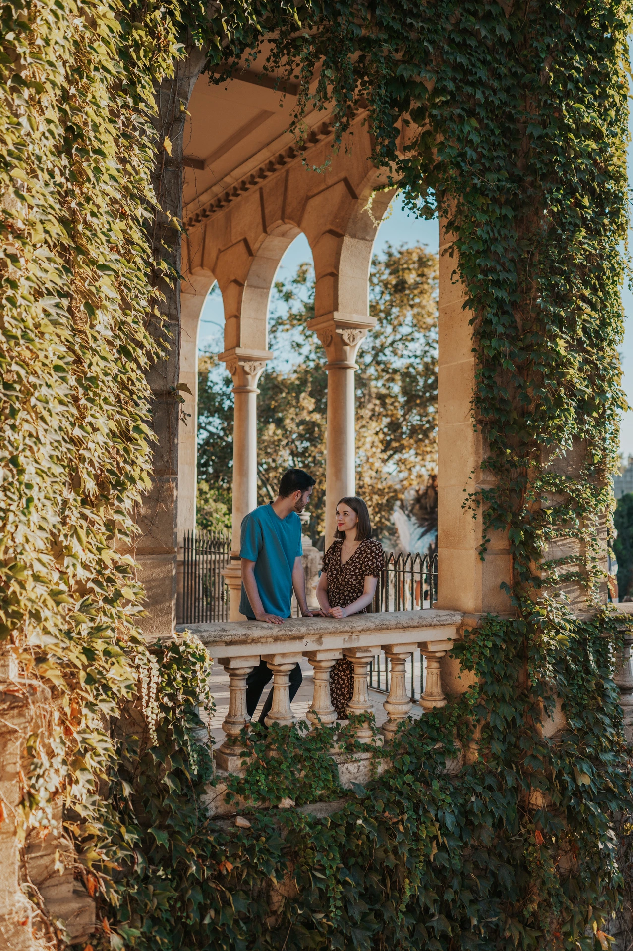 The couple framed by ivy and stone arches above a carved balustrade during their couple photoshoot in Barcelona.