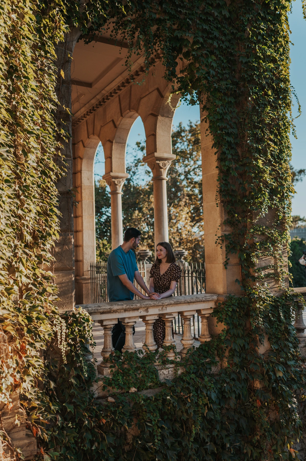 The couple framed by ivy and stone arches above a carved balustrade during their couple photoshoot in Barcelona.