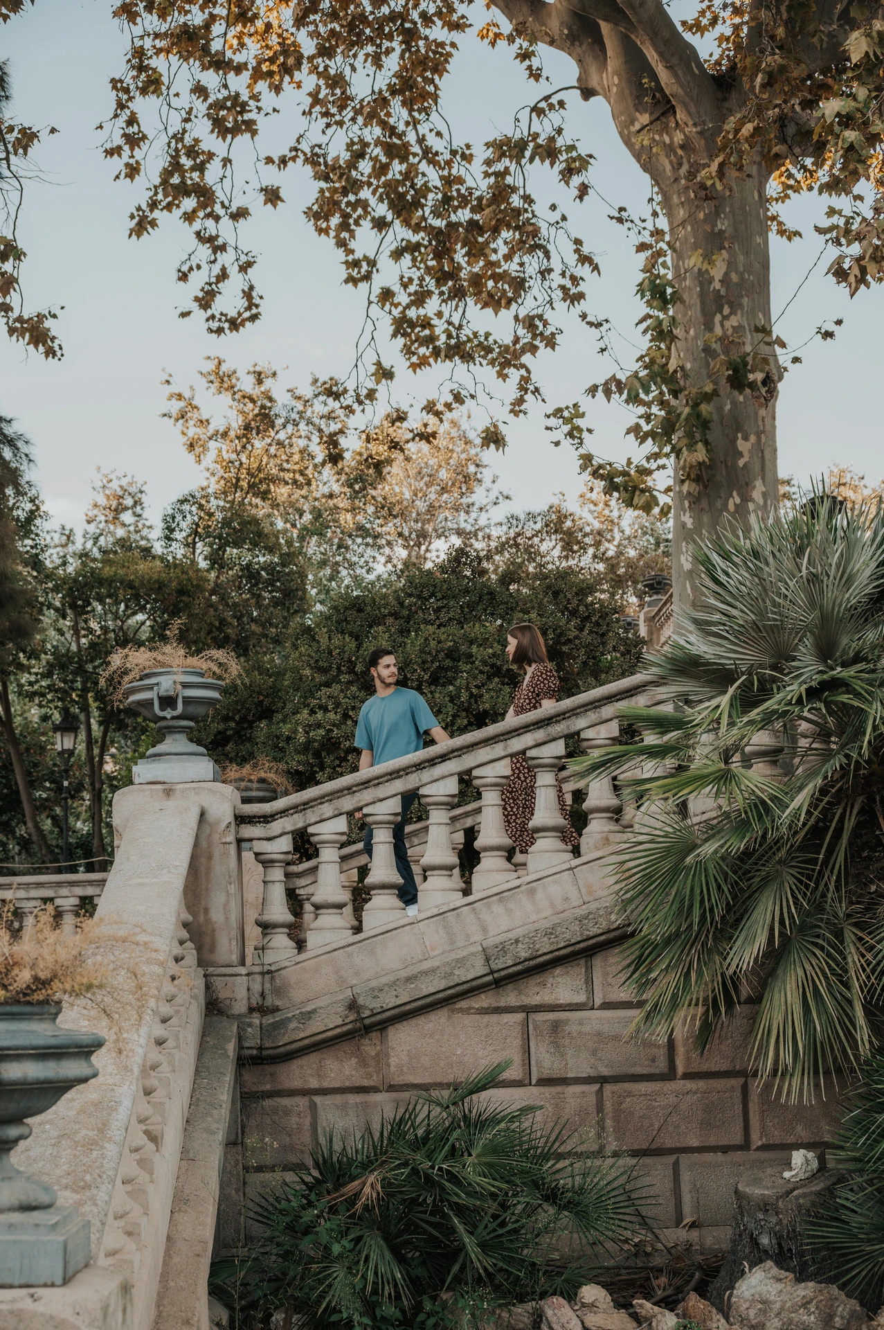 A wide view of the couple on the park staircase among trees and greenery during their couple photoshoot in Barcelona.