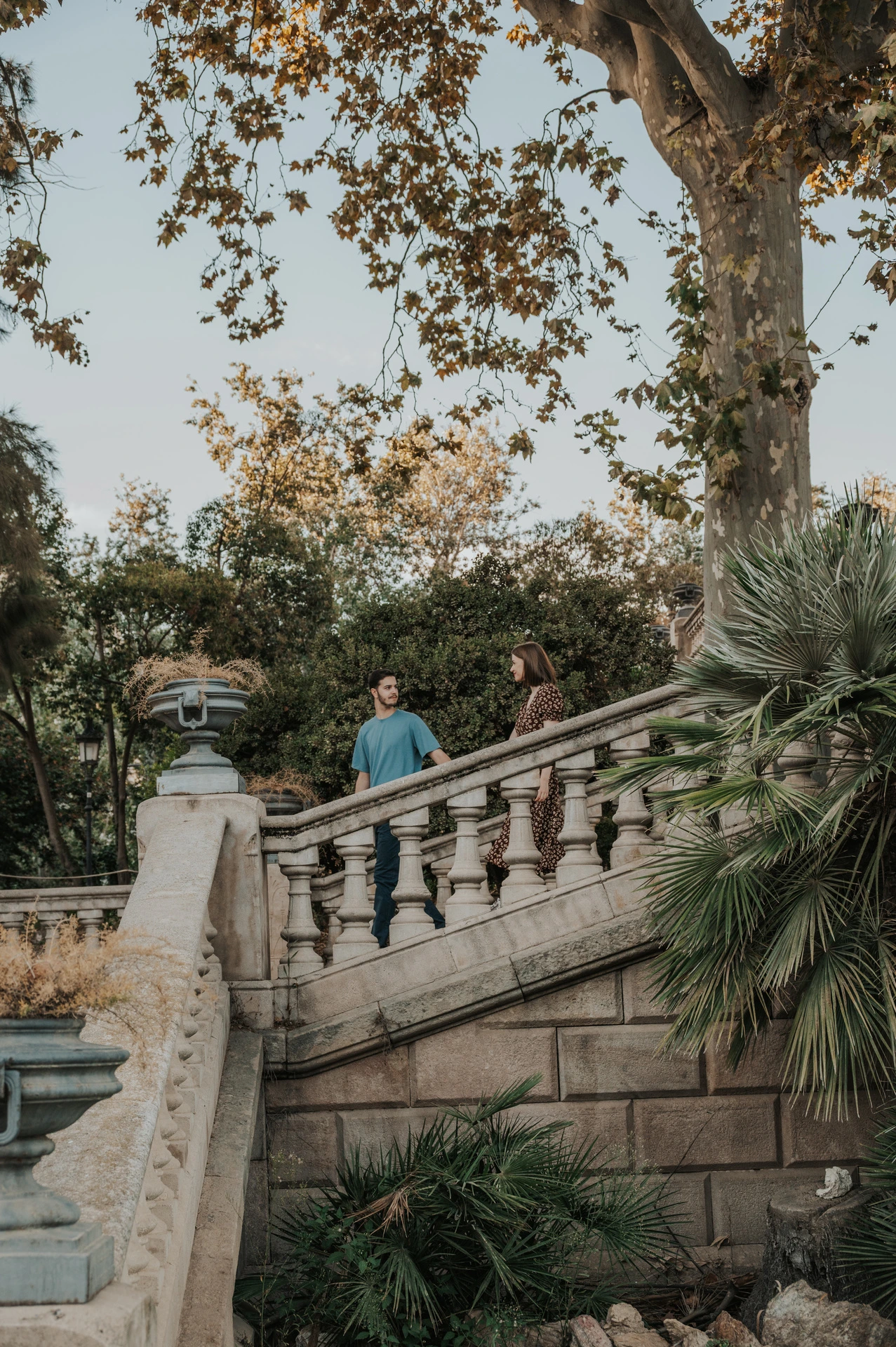 A wide view of the couple on the park staircase among trees and greenery during their couple photoshoot in Barcelona.