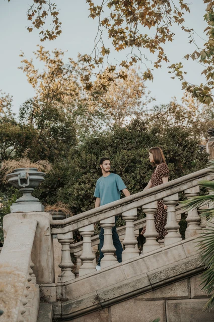 Together on the stone staircase | Barcelona couple photoshoot The couple standing close together on a stone staircase beneath leafy trees during their couple photoshoot in Barcelona.